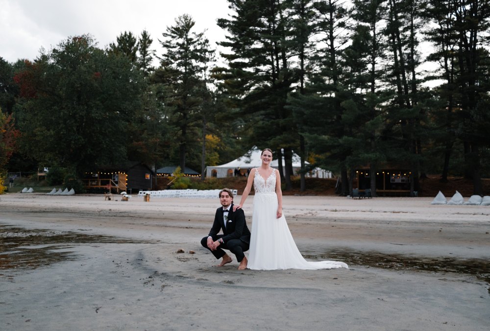 Paige agenouillée pieds nus près de Greg sur le sable à Anupaya Cabin Co., les grands pins derrière